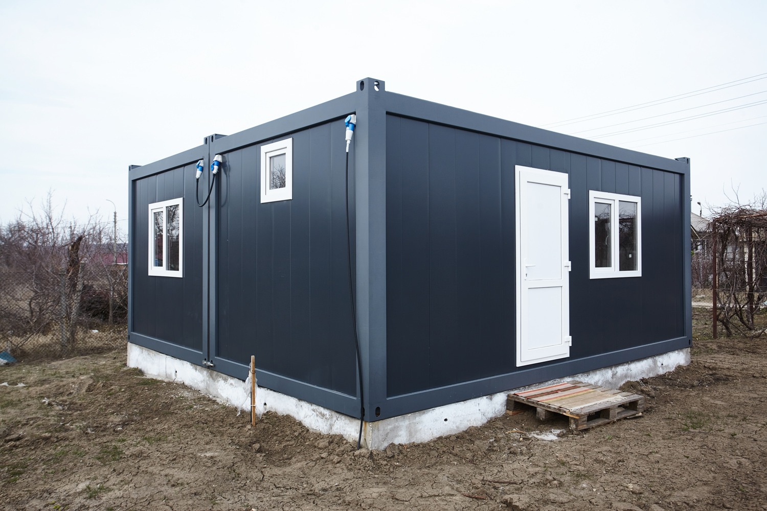 Imaginea prezintă un complex de construcții modulare, incluzând containere transformate în case moderne, amplasate pe un teren verde, evidențiind eficiența și versatilitatea soluțiilor de locuit alternative.