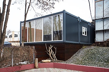 Imaginea prezintă o construcție modulară modernă realizată din containere, evidențiind o casă inovatoare și eficientă din punct de vedere energetic, cu un design atrăgător și functional.