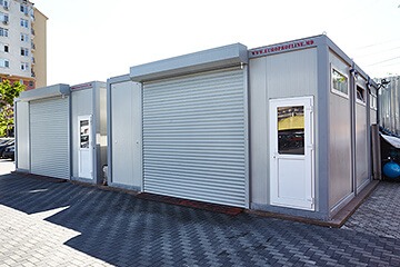 Imagine a unor construcții modulare din containere, prezentând case moderne și funcționale, cu design minimalist și integrare armonioasă în peisajul înconjurător.